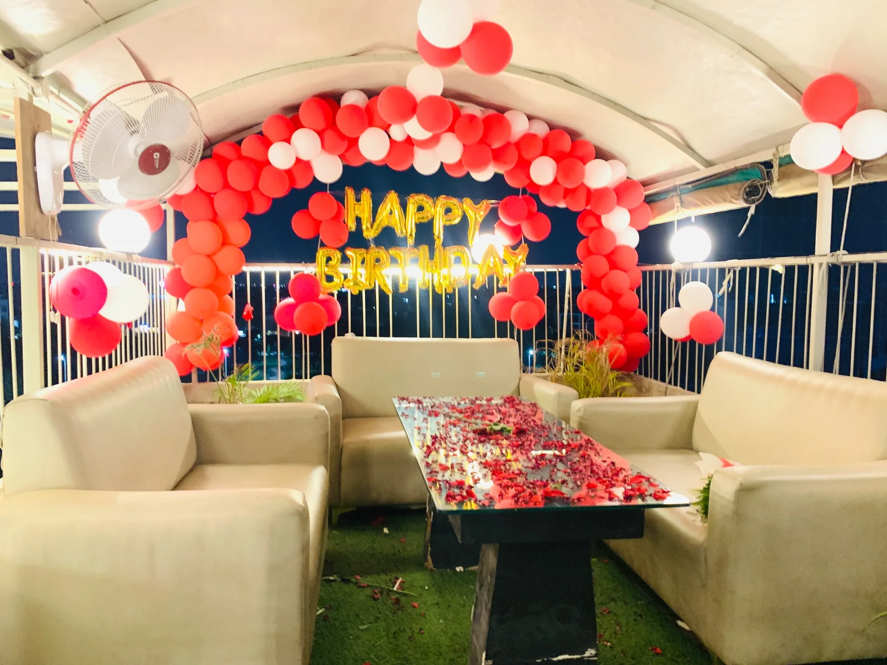 Red and white birthday balloons beside sofa seating on the Chairish Cafe semi rooftop in Malviya Nagar